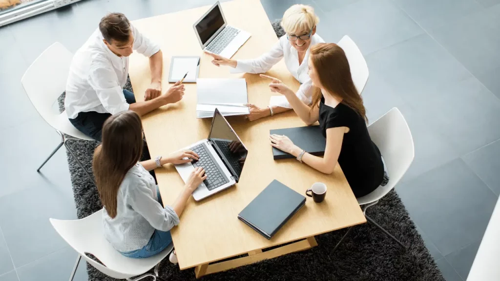 Imagem mostra um grupo de pessoas, homens e mulheres, reunidos com notebooks em um ambiente empresarial.